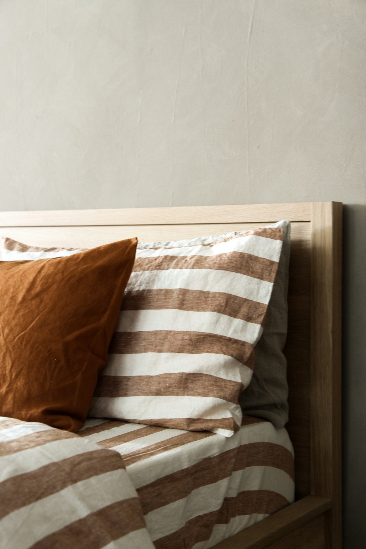 Close detail of layered linen bedding in rust and cream against a timber headboard